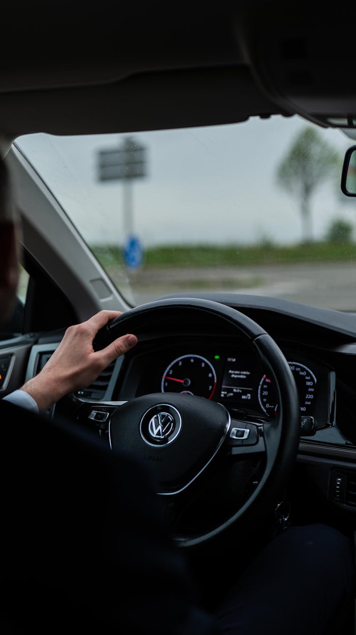 View from driver's seat showing car dashboard and steering wheel. Outdoors scene.